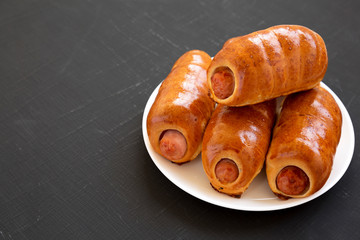 Homemade beef sausage kolache on a white plate on a black background, side view. Copy space.