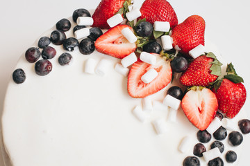 A cake with white frosting, straberries and blueberries
