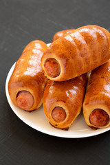 Homemade beef sausage kolache on a white plate on a black surface,  side view. Close-up.