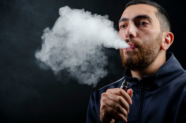 vape and smoke vape electronic e-cigarette or e-cig by a young man with smoke clouds over a black...