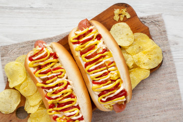 Homemade colombian hot dogs with pineapple sauce, yellow mustard and mayo ketchup on a rustic wooden board, overhead view. Flat lay, top view, from above. Close-up.