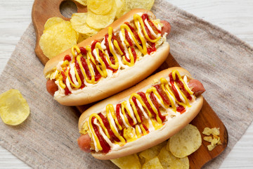 Homemade colombian hot dogs with pineapple sauce, yellow mustard and mayo ketchup on a rustic wooden board, top view. Flat lay, from above, overhead. Close-up.