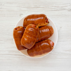 Homemade beef sausage kolache on a white plate on a white wooden background, top view. Flat lay, overhead, from above. Close-up.