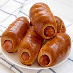 Homemade beef sausage kolache on a white plate on a white wooden surface, side view. Close-up.