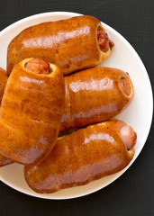 Top view, homemade beef sausage kolache on a white plate on a black surface. Flat lay, overhead, from above. Close-up.