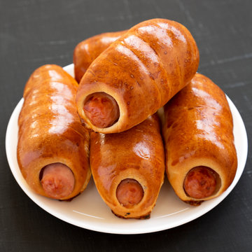 Homemade beef sausage kolache on a white plate on a black background, side view. Close-up.