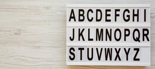 English alphabet on a modern board over white wooden surface, top view. Letters from A to Z. Back...