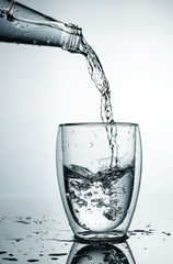 Fresh and cold, pure Water is poured into a glass. Purified water in a glass on a gray background. Motion freeze splash of crystal water on grey background.