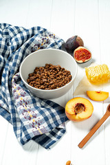 Chocolate granola in a white bowl in a composition with honeycombs, a spoon, figs and peach. Healthy breakfast food. Making breakfast. Gluten free