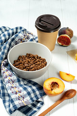 Chocolate granola in a white bowl in a composition with honeycombs, a spoon, figs and peach. Healthy breakfast food. Making breakfast. Gluten free