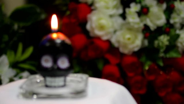 Mexican candle in the form of a skull burns against a background of flowers with a change in depth of field