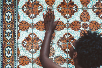 Rearview of a black girl with nail-art placing her hand and touching textured pattern of a wall in Portugal with a traditional azulejo ornament on it