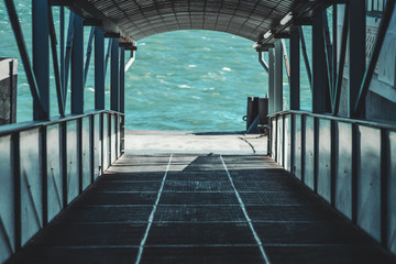 Сovered descending boarding gate corridor on the quay with plenty of beams for passengers of a boat or a ship, with river water in the background, selective focus in a middle, shallow depth of field