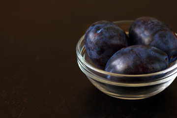 Plums blue prune in a glass bowl on a dark countertop.
