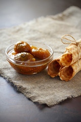 Waffle rolls three pieces tied with rope and Fig jam in a glass bowl on burlap and on dark countertop.