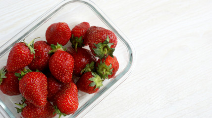 bright big sweet delicious fragrant red strawberry berries in a glass plate on a wooden table on a Sunny summer day.