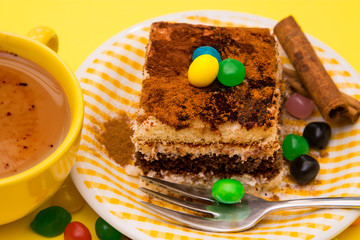 Tiramisu dish with cinnamon and candies on yellow background