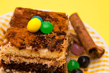 Tiramisu dish with cinnamon and candies on yellow background