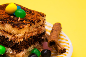 Tiramisu dish with cinnamon and candies on yellow background
