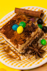 Tiramisu dish with cinnamon and candies on yellow background