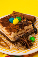Tiramisu dish with cinnamon and candies on yellow background