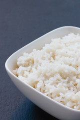 gekochter Reis in einer weißen Schale auf schwarzem Schiefer