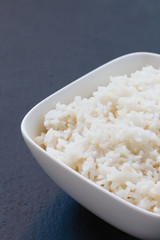 gekochter Reis in einer weißen Schale auf schwarzem Schiefer