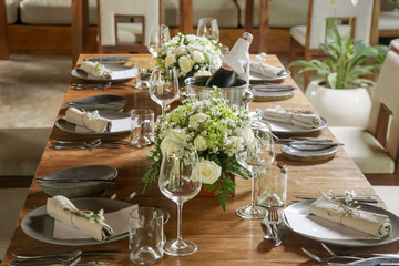 The beautiful arrangement on the wooden table, white roses and ceramic plates. Boho chic wedding table setting. 