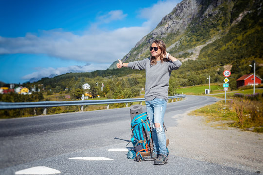 happy girl traveler with a backpack on the road in Norway, traveling to northern Europe, adventure hiking hitchhiking
