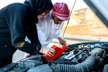 Arabic woman and her husband pouring oil in the car engine