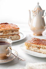 A slice of homemade chicken and sesame pie. On a white plate. Near a coffee pot and a cup of coffee. White background