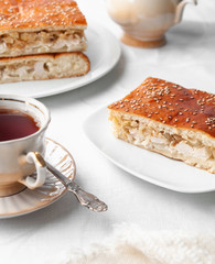 A slice of homemade chicken and sesame pie. On a white plate. Near a coffee pot and a cup of coffee. White background.