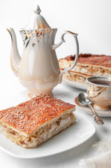 A slice of homemade chicken and sesame pie. On a white plate. Near a coffee pot and a cup of coffee. White background