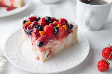 A piece of home-made cottage cheese berry pie. Garnished with cream, strawberries, blueberries, sea buckthorn berries. On a white plate. Close-up. White background. 