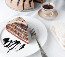 A slice of marble cake with cream. Garnished with icing and chocolate. On a white plate with a fork. Close-up.