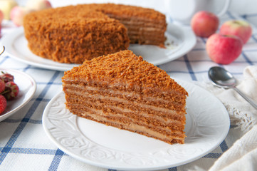 A slice of homemade multilayer honey cake. Orange color. On a white plate. Close-up. Testura. Nearby are berries, apples and cake. Tablecloth in a rustic style.