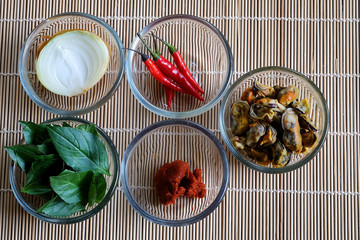 Set of important ingredients for making Stir Fried Mussels with Thai Basil and Chili on wood mat and space for write wording containing Mussels, Onion, Red Chili Paste, Chili and Thai Basil leaves