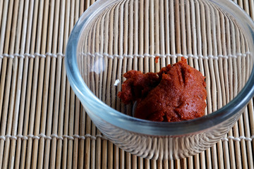 Red curry chili paste in clear glass cup on wood mat and space for write wording, important ingredient secret recipe for making delicious spice curry, mixing many kind of herb and vegetable