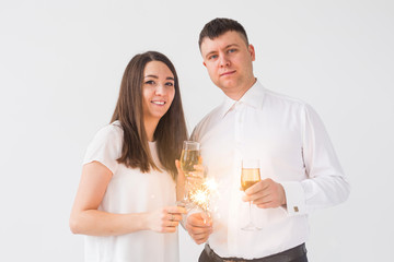New year, holidays, date and valentines day concept - Loving couple holding sparklers light and glasses of champagne over white background