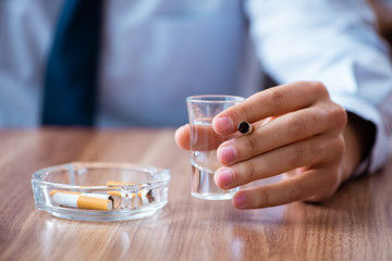 Male employee drinking vodka and smoking cigarettes at workplace