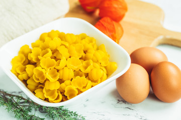 Pâtes crues dans bol blanc et oeufs sur la table de cuisine