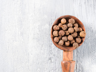 Allspice (Jamaica pepper) on a wooden spoon on a gray background vertically