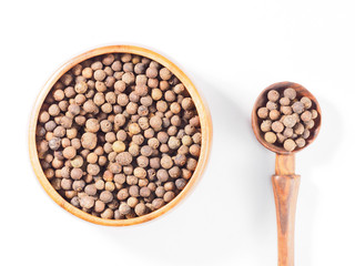 Allspice (Jamaica pepper) in the wooden cup and spoon vertically on white background