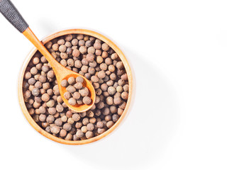 Allspice (Jamaica pepper) in the wooden cup and spoon diagonally on white background
