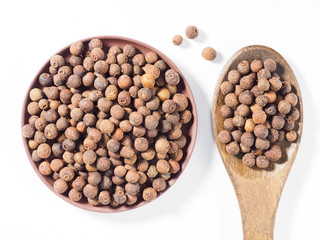 Allspice (Jamaica pepper) in clay plate and wooden spoon vertically on white background