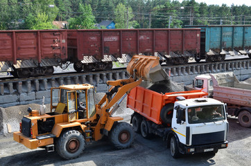 Wheel loader loads gravel into a dump truck at a cargo railway station. Fron-end loader unloads crushed stone in a gravel pit.  Unloading bulk cargo from freight cars on high railway platform