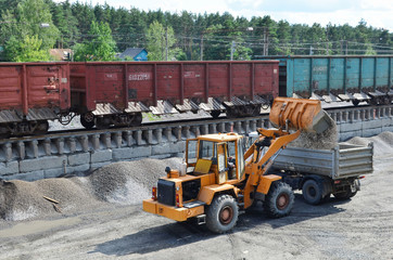 Wheel loader loads gravel into a dump truck at a cargo railway station. Fron-end loader unloads crushed stone in a gravel pit.  Unloading bulk cargo from freight cars on high railway platform