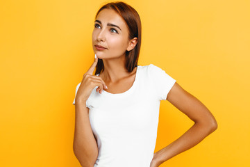 Serious thoughtful young woman thinking on yellow background