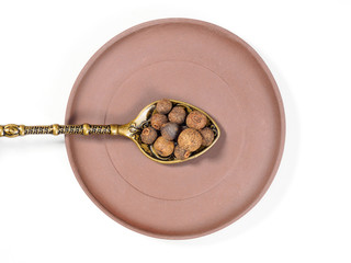 Allspice (Jamaica pepper) in clay plate and metal spoon on white background