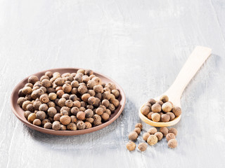 Allspice (Jamaica pepper) in clay plate and wooden spoon diagonally on grey cement background